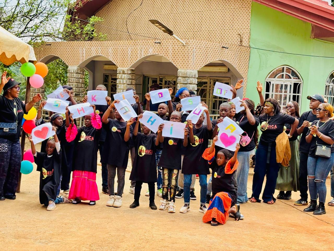 Children and staff holding SHAHICA signs at a day camp in Cameroon